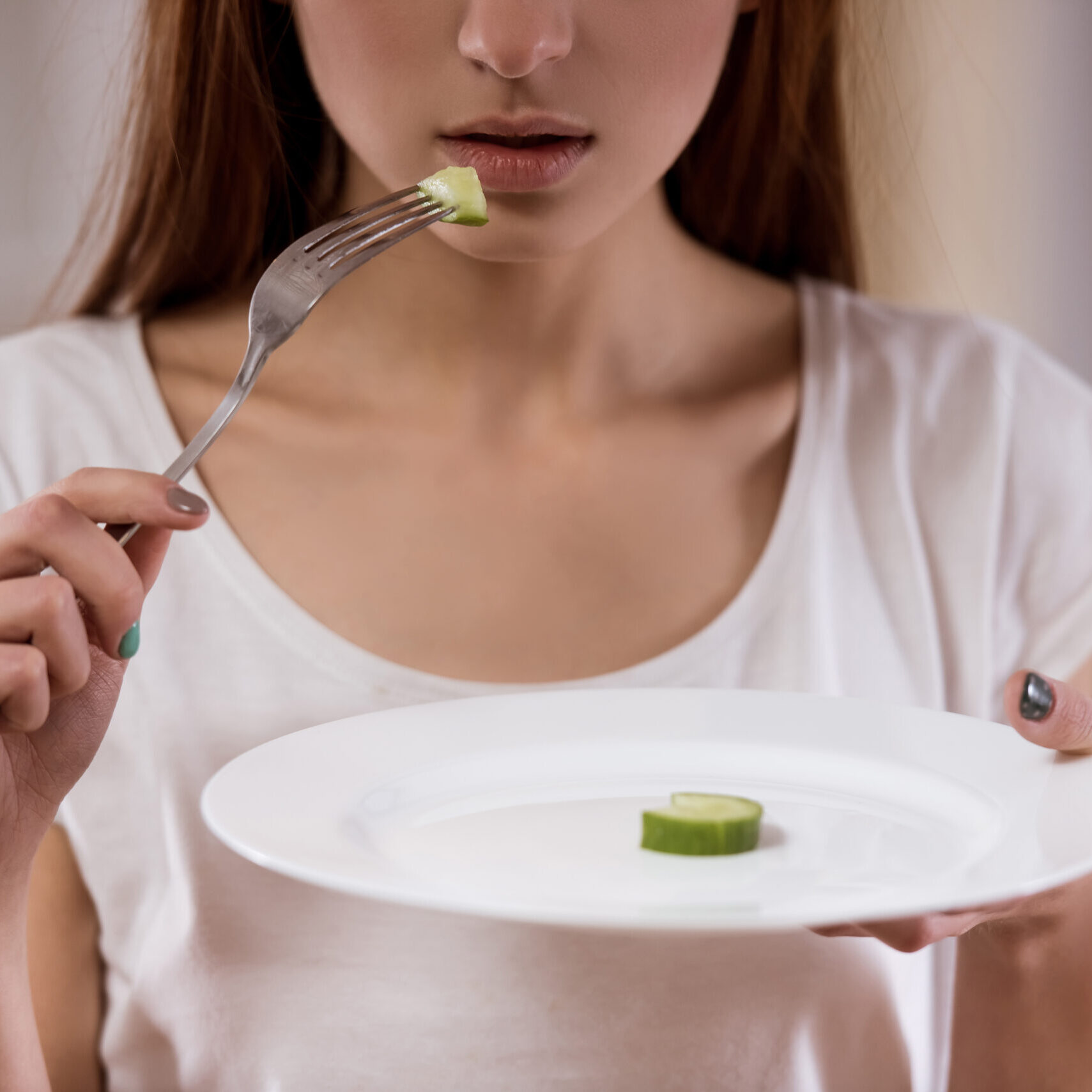 Thin girl with an empty plate standing in the center of the room closeup, malnutrition harms health.